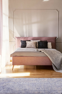 毛毯和枕头在粉红色的床上，简单的卧室内部，地毯和墙壁与成型。 真实照片