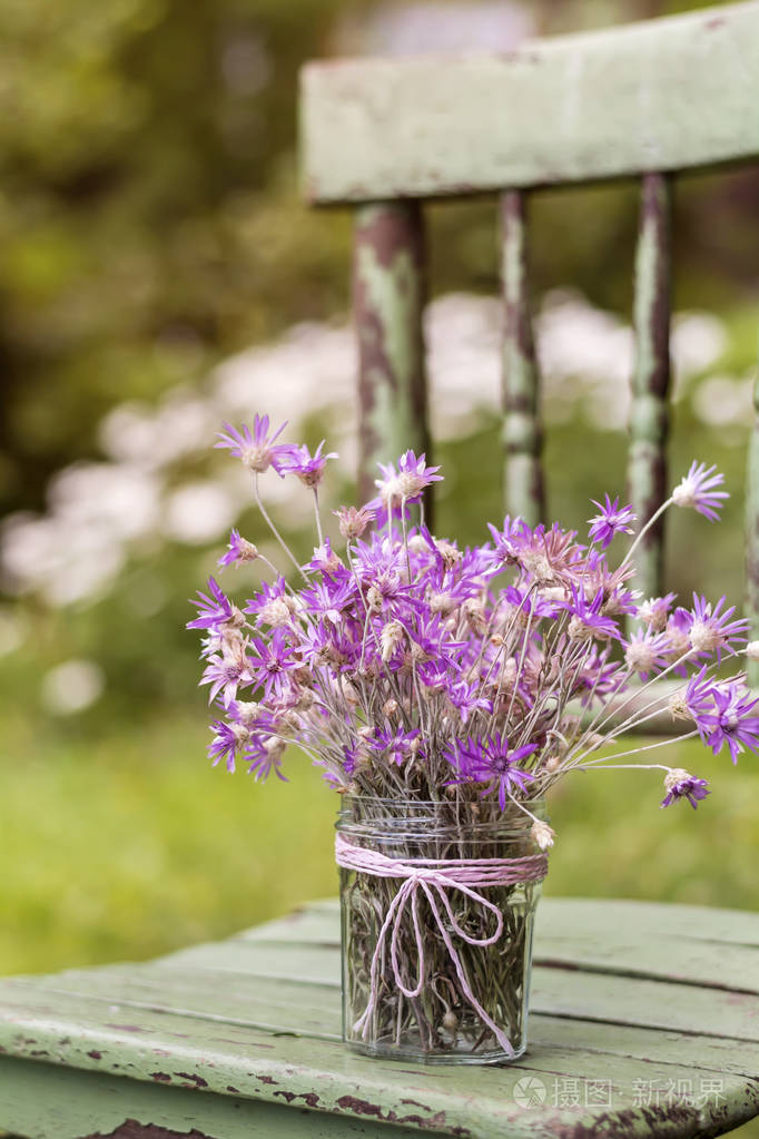 一把漂亮的粉红色花放在木椅上的罐子里