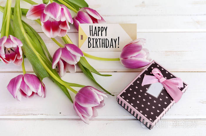 木制背景的郁金香花，带有生日快乐卡和礼品盒