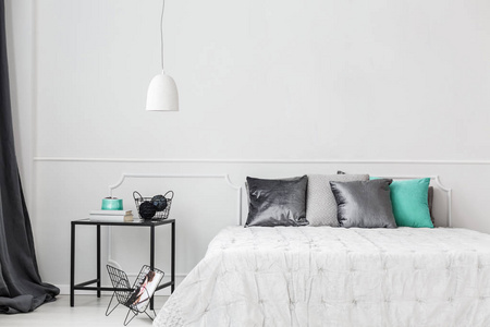 缎子枕头在极简主义的床上，白色的空墙在时髦的卧室内部，灰色和茶绿色装饰。