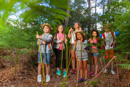 一群孩子站在森林里，在徒步旅行中休息，手里拿着手工制作的登山杆竹竿鬃毛