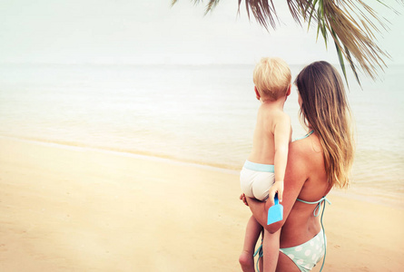 美丽的母亲和婴儿站在海滩前看大海的后视镜