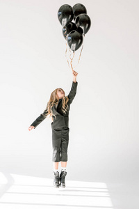 梦幻般的小孩用灰色的黑气球跳跃或飞行