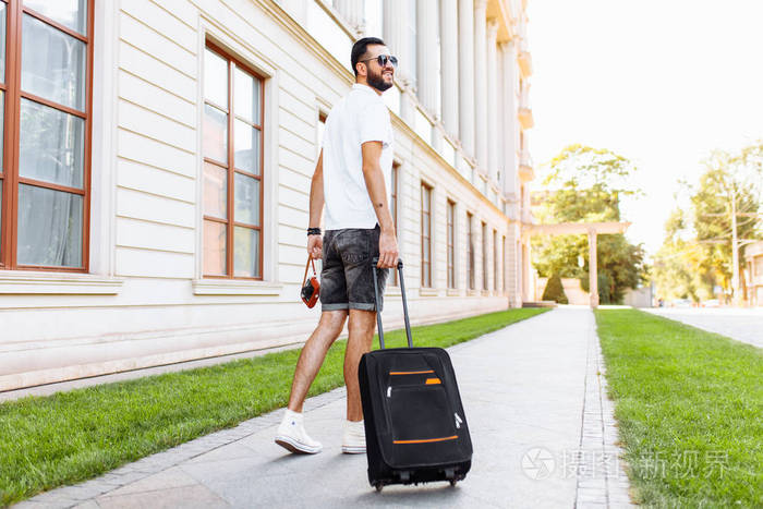 年轻的时髦男徒步旅行者带着手提箱和照相机在我脖子上走来走去