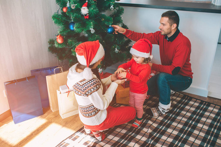 圣诞快乐, 新年愉快。迷人的可爱和漂亮的家庭图片。他们装饰圣诞树。年轻女子抱着小女孩的玩具。男人把蓝色的玩具放在树上