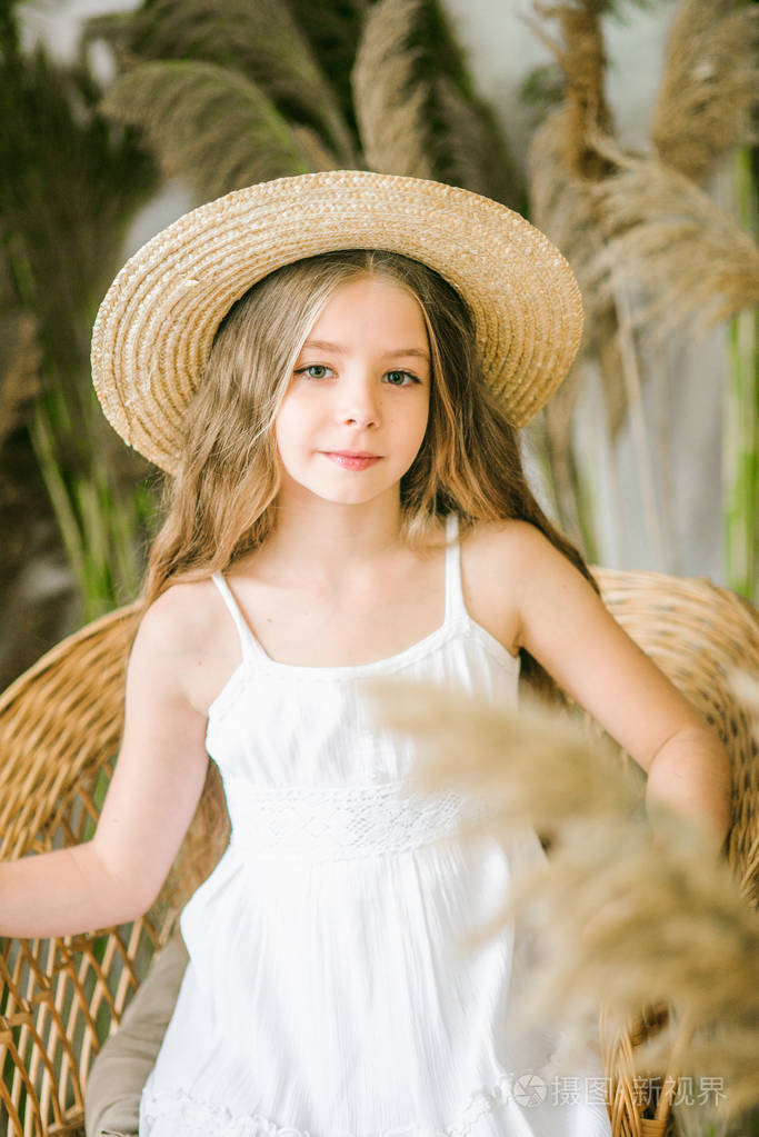 一个可爱的小女孩长着一头金色的长发穿着白色的沙拉帆戴着一顶草帽坐