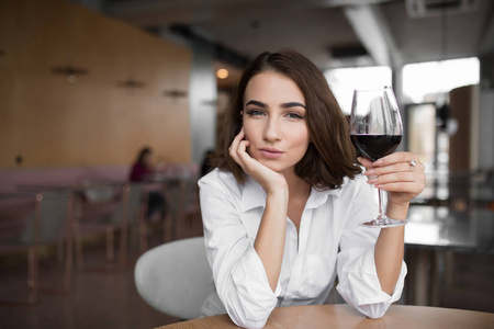 年轻女子端着红酒杯坐在餐厅里，头靠在手上