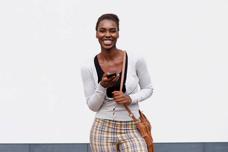 年轻黑人妇女的正面肖像，带着手机和手提包微笑