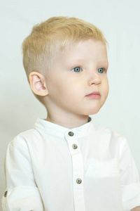 一个有着蓝色眼睛和白色背景的金发的严肃可爱男孩的肖像。