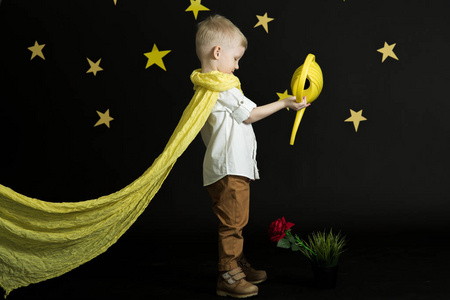 一个戴着黄色围巾的小男孩在夜空中，星星在用黄色浇水罐浇红玫瑰