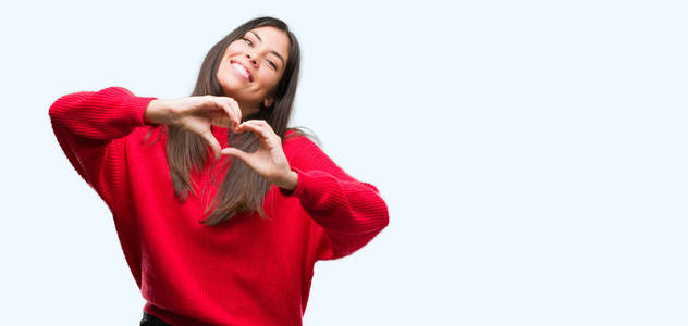 年轻漂亮的西班牙裔，穿着红色毛衣，微笑着，爱着，用手展示着心的象征和形状。 浪漫的概念。
