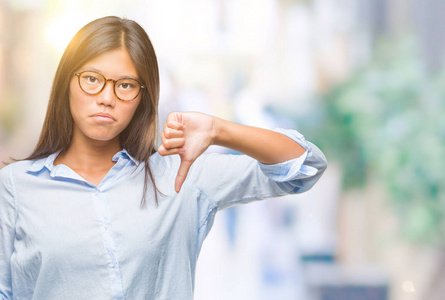 年轻的亚洲女人在孤立的背景上显示智能手机空白屏幕，愤怒的脸，消极的迹象，显示不喜欢，拇指向下拒绝概念