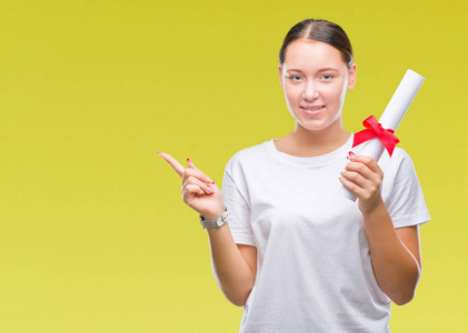 年轻的白种人女人在孤立的背景上持有学位，非常高兴地用手和手指指向一边