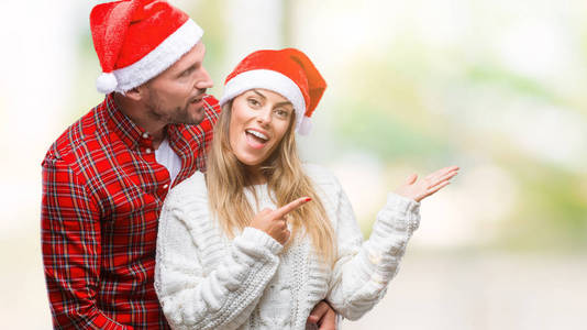 恋爱中的年轻夫妇戴着圣诞帽，戴着孤立的背景，惊讶地微笑着对着相机，用手和手指指点。