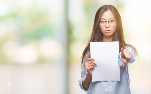 年轻的亚洲女人拿着白纸在孤立的背景上，手指着相机，向你手势正面和自信的手势