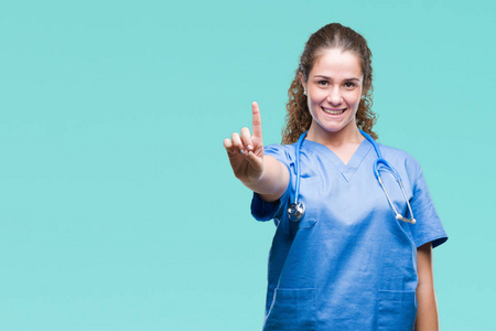 年轻的黑发医生女孩穿着护士或外科医生制服，在孤立的背景上显示和指向第一手指，同时微笑自信和快乐。