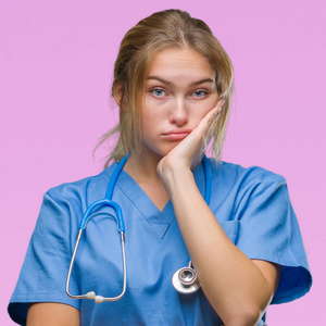 年轻的高加索医生女人穿着外科医生制服，在孤立的背景下思考，看起来疲惫，厌倦了交叉双臂的抑郁问题。