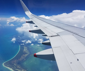 在墨西哥的里维埃拉玛雅上空飞行的飞机机翼，云层在加勒比海海岸和蓝色水域之上。