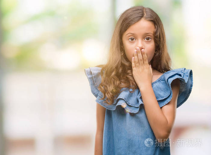 深褐色头发的西班牙女孩穿着牛仔裙用手捂住嘴羞愧地