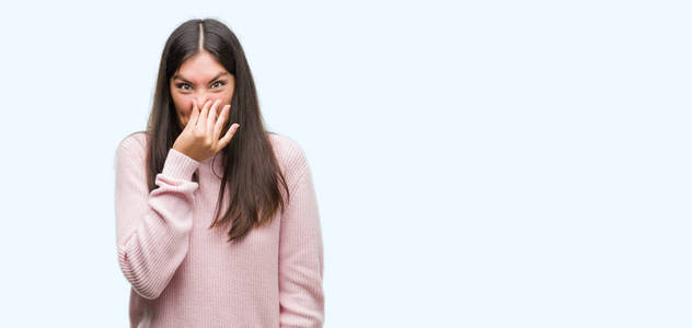 年轻漂亮的西班牙裔女人穿着一件毛衣，闻着一些臭味和令人恶心的难以忍受的气味，用手指在鼻子上屏住呼吸。 难闻的概念。