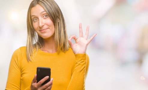 年轻漂亮的女人用智能手机在孤立的背景下发送信息，做OK标志，手指，优秀的符号