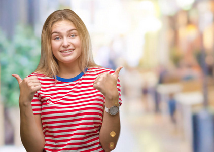 年轻的高加索女人在孤立的背景下成功的标志，用手竖起大拇指，微笑和快乐地做积极的手势。 用欢快的表情看着相机，胜利者的手势。