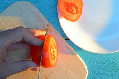 在一个白色的陶瓷盘子旁边的蓝色绿松石桌子上切番茄