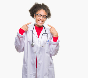 年轻的非洲美国医生女人在孤立的背景上微笑，自信地展示和指着手指，牙齿和嘴。 健康概念。