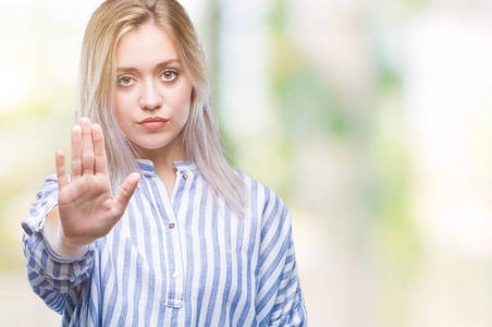 年轻的金发女人在孤立的背景下做停止用手掌唱歌。 警告表情，脸上有负面和严肃的手势。