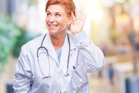 高级白种人医生女士穿着医疗制服，在孤立的背景下微笑，用手捂住耳朵听谣言或流言蜚语。 耳聋概念。
