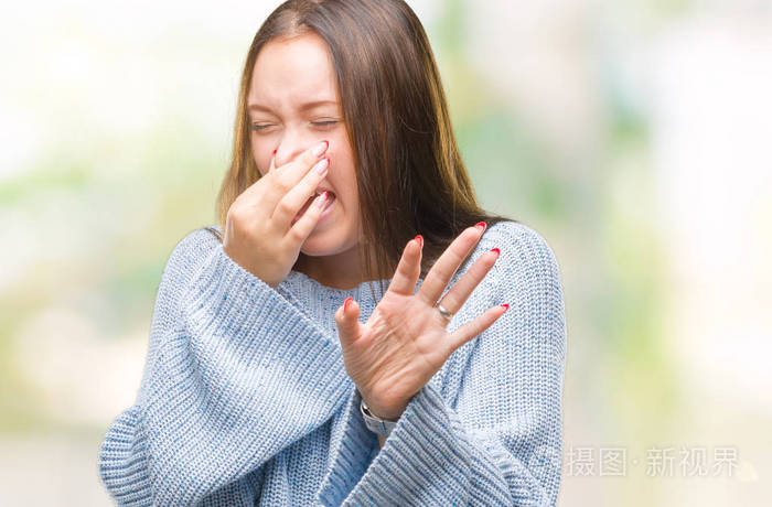 年轻美丽的白种人女人穿着冬天的毛衣,在孤立的背景上闻着一些臭味和