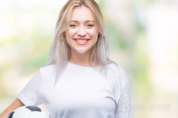 在孤立的背景上捧着足球,脸上挂着快乐的表情,微笑着露出自信的牙齿