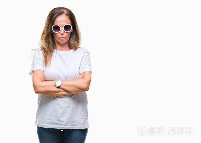 中年西班牙裔女人戴着时尚太阳镜，超越了孤立的背景怀疑论者，紧张的不赞成表情在脸上交叉的手臂。 消极的人。