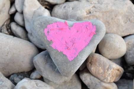 在许多小石头的背景上涂上口红的粉红色心脏