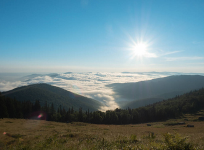 夏天在山地牧场日出。喀尔巴阡山山脉, 西乌克兰。低白云在范围之间流动。蓝天下升起的太阳。乌克兰自然风景。背景模糊