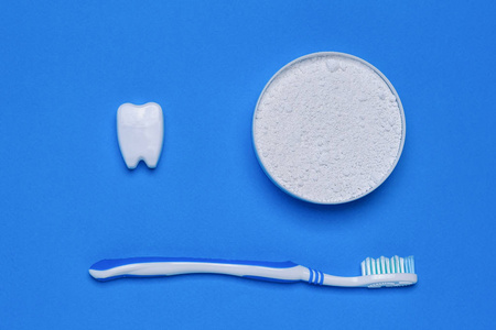 一罐牙齿清洁粉一支蓝色牙刷和一个蓝色桌子上的牙齿雕像。 口腔护理产品。 从顶部的视图。 平躺着。