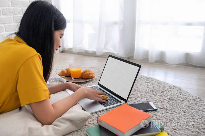 亚洲女性自由职业者在家里用手提电脑工作女人躺在砖墙的地毯上