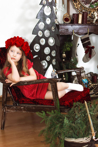 穿红衣服戴帽子的女孩坐在圣诞装饰的房间里的椅子上