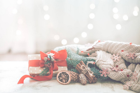 圣诞节舒适在一个房间的灯光背景上，有一棵圣诞树的灯光和树枝，桌子上有一个红色蝴蝶结的礼物，供文字使用
