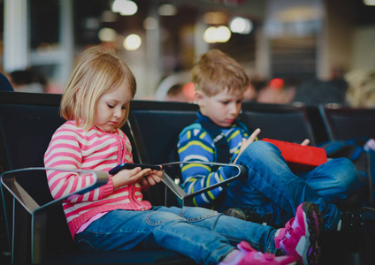 男孩和女孩看触摸垫和移动电话在机场