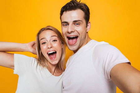 照片快乐兴奋的年轻情侣站在黄墙背景上，用相机自拍。