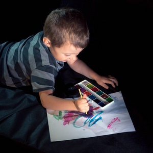 孩子在纸上画水彩画。 黑暗的背景。