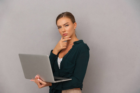 体贴的年轻女商人站在灰色背景下，在笔记本电脑上工作