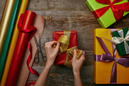 在木制表面包裹的圣诞礼物和其他礼物上绑丝带的女人剪的照片