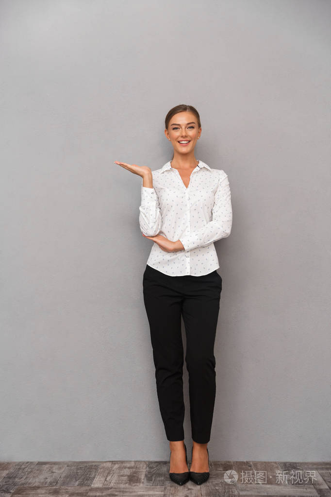 美丽的商业女性的形象站在灰色的墙壁背景上摆姿势显示着共同的空间