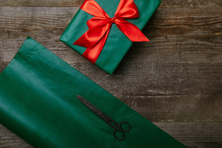 绿色包装纸剪刀的顶部视图，并在木制背景上呈现红色丝带