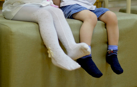 穿着白色连裤袜的女孩和坐在搁脚凳旁边的穿短裤和袜子的男孩的腿照片