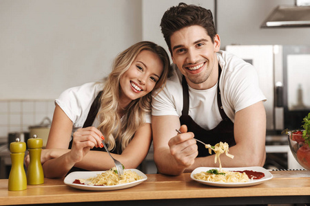 快乐兴奋的年轻朋友的形象，爱夫妇厨师在厨房吃美味的意大利面。