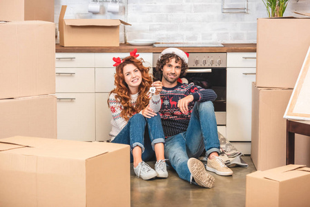 幸福的年轻夫妇在圣诞节的时候坐在新公寓里，拿着钥匙对着镜头微笑