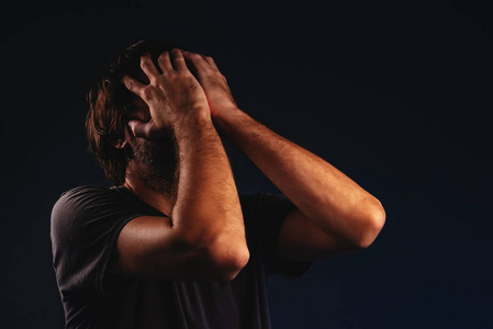 男人绝望地哭泣,双手捂脸,低键肖像照片